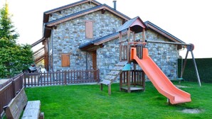 A stone building with a wooden play area including a slide and swings.
