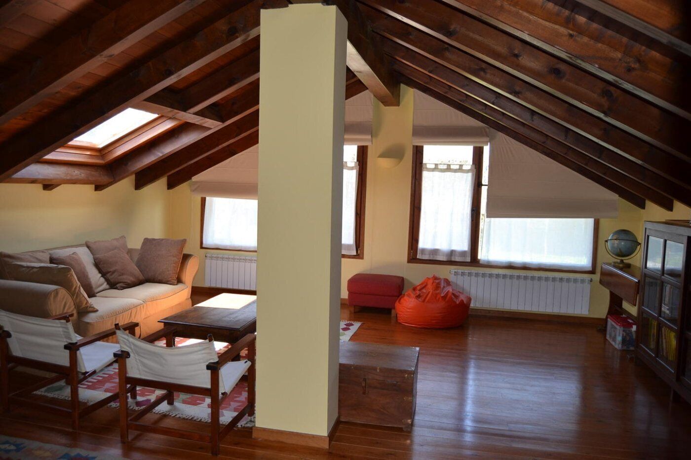 A loft-style room with a wooden ceiling, a sofa, a small table, a red bean bag, and a globe on a shelf.