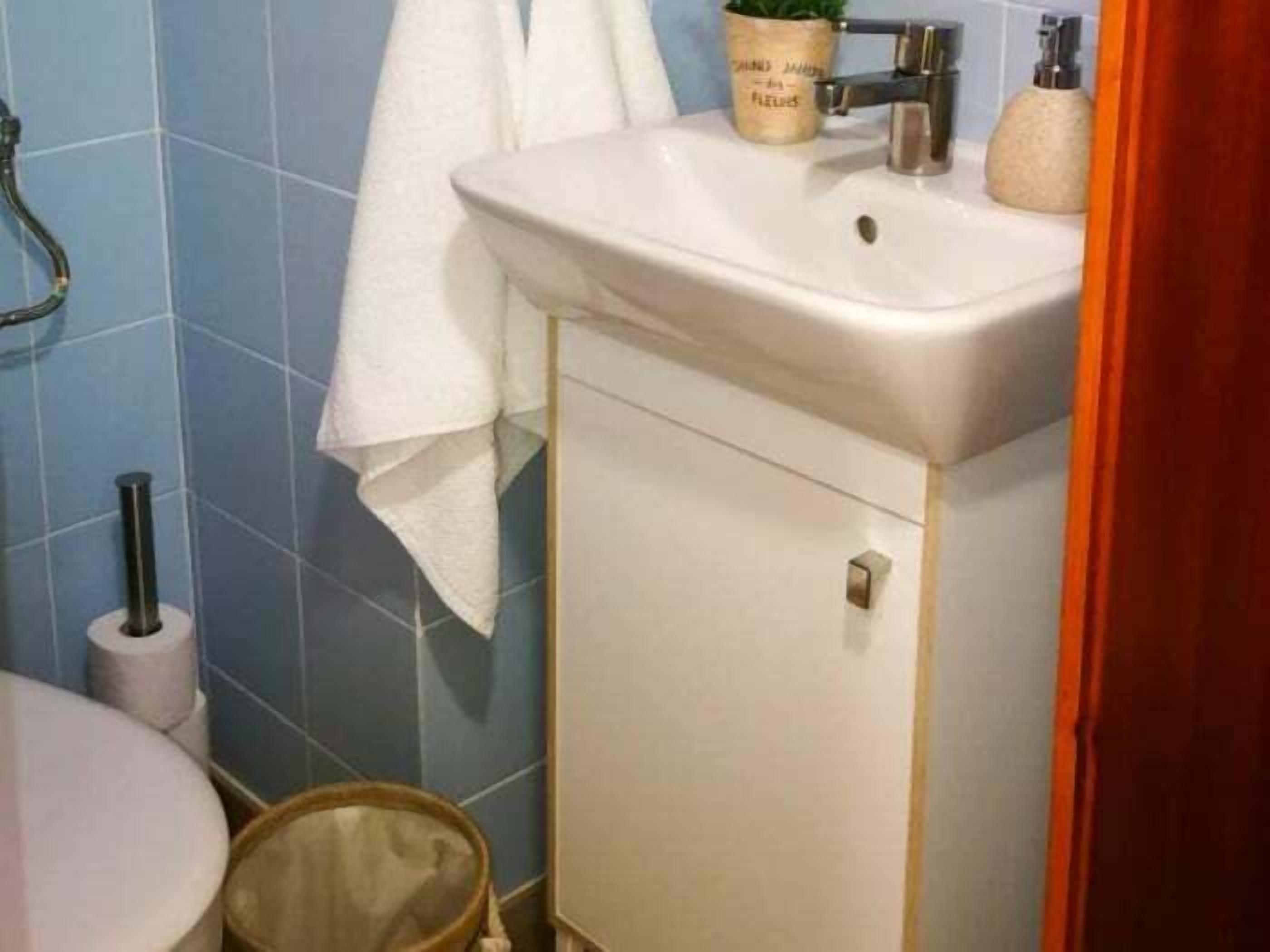 A bathroom with a white sink, blue tiles, a toilet, and a small trash bin.