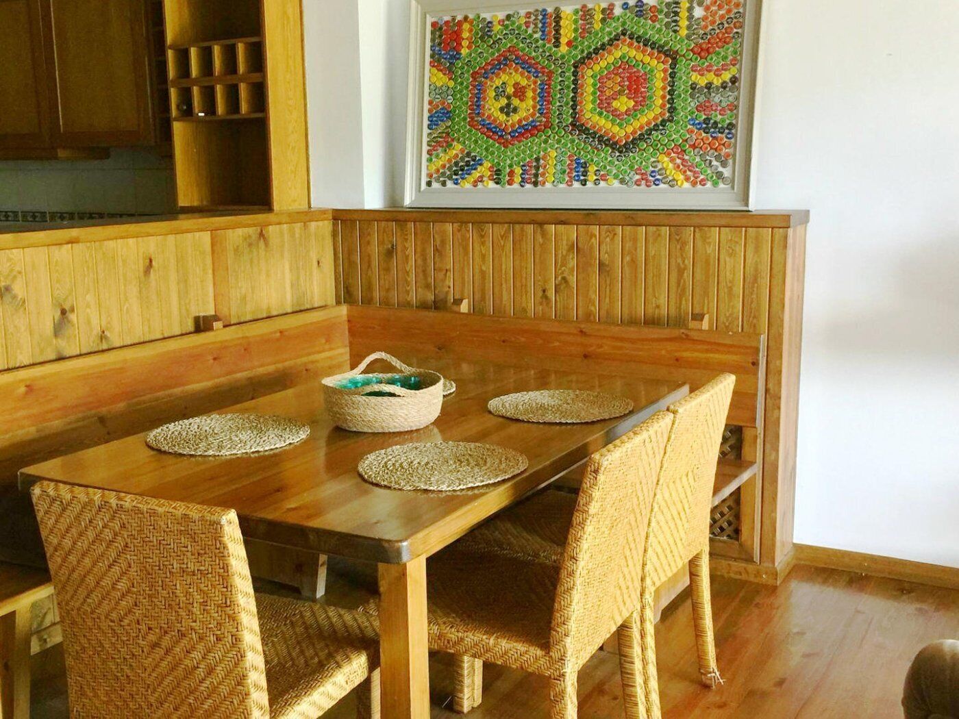 A wooden dining table with woven chairs, a woven placemat, and a woven basket with a blue item on it.