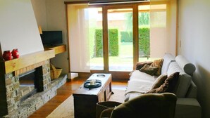 A cozy living room with a stone fireplace, a sofa, a coffee table, and a television. - Ground Floor 3 rooms Pool, Fireplace, Private Garden & Views (Olopte)