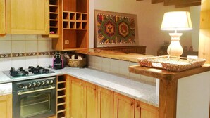 A kitchen with wooden cabinets, a gas stove, an oven, a decorative wall piece, and a table lamp. - Ground Floor 3 rooms Pool, Fireplace, Private Garden & Views (Olopte)