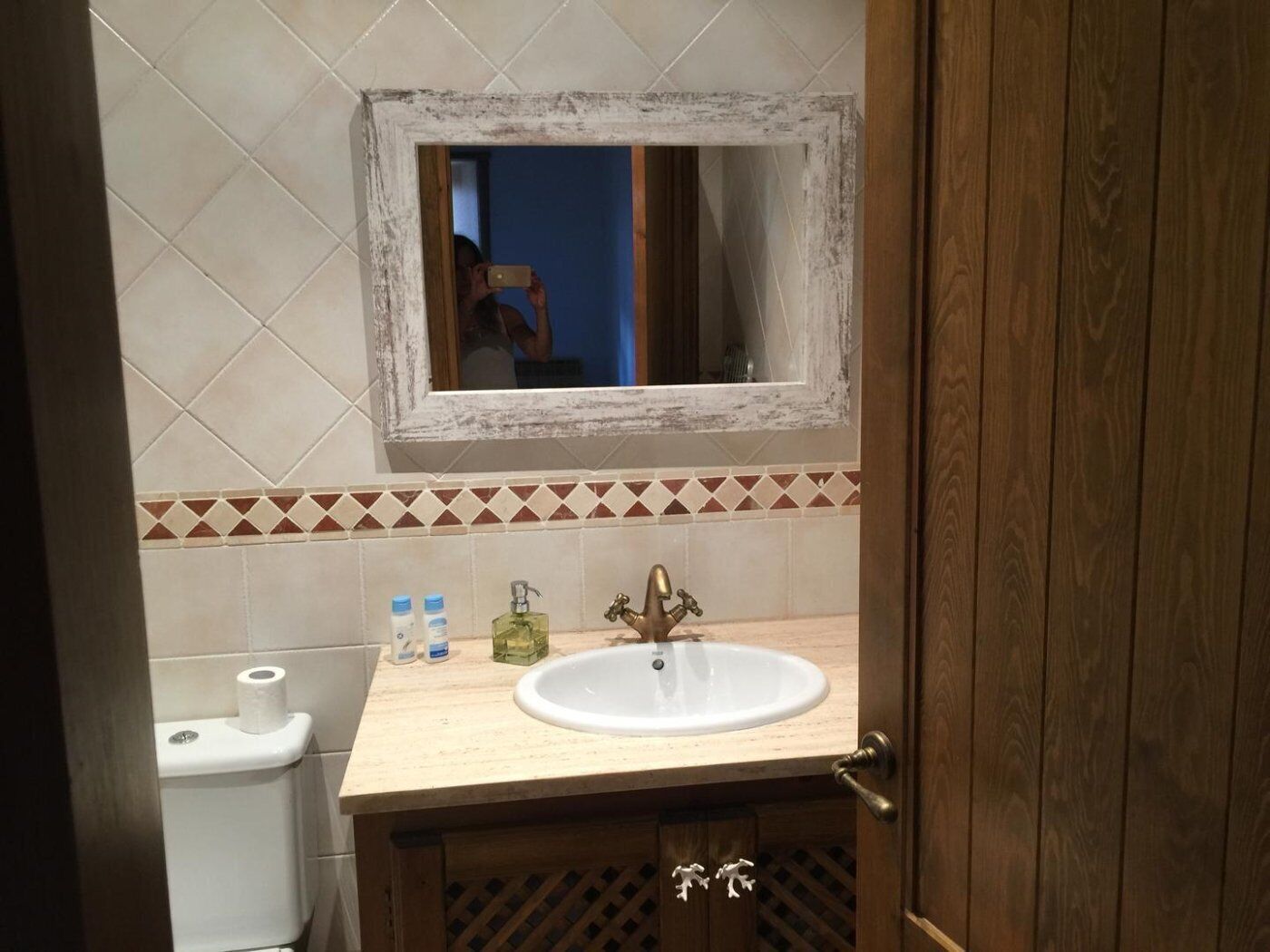 A bathroom with a wooden vanity, a white sink, a mirror, and a toilet.