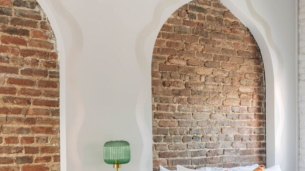 A hotel room with two beds, a brick wall, and a green lamp on a wooden table. - Bellwether House Summ (Louisville)
