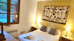 Quarto de hotel com cama, duas mesas de cabeceira com luminárias, uma janela e uma obra de arte na parede.