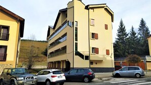 Un immeuble à plusieurs étages, doté d’une façade beige, de nombreux balcons et d’un parking où sont stationnées plusieurs voitures.