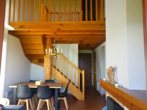 Un espace repas agrémenté d’un escalier en bois, d’un lustre et d’une vue sur une autre pièce.