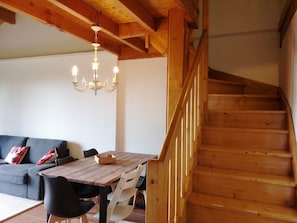 A wooden staircase leading to an upper level, a dining table with chairs, a sofa with cushions, and a chandelier.
