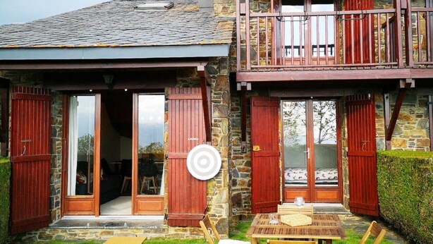 Une maison en pierre à deux étages, dotée de volets en bois, d’un balcon et d’une terrasse avec une table et des chaises.
