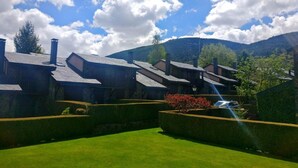 Un bâtiment traditionnel en pierre, doté de plusieurs cheminées, entouré de haies bien entretenues et d’une pelouse verdoyante.