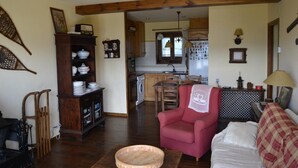 A cozy living room with a red armchair, a wooden cabinet with dishes, and a dining area with a table and chairs. - Apartment 3 rooms Fireplace, Private Garden & Cadí Views (Ger)