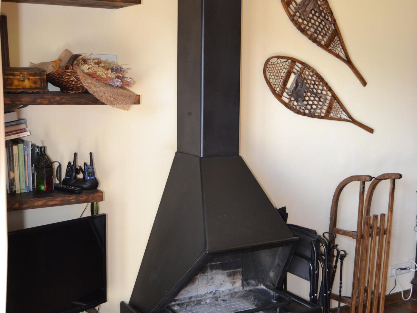 A room with a fireplace, a television, and a shelf with books and a bottle.
