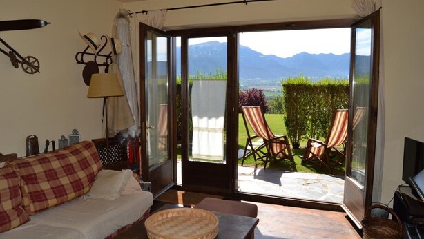 A cozy room with a sofa, a table, and a view of a garden with chairs. - Apartment 3 rooms Fireplace, Private Garden & Cadí Views (Ger)
