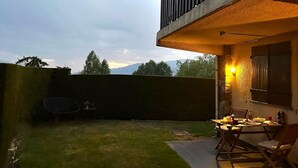 A patio area with a table and chairs, a small table with a chair, and a wall-mounted light fixture. - Ground Floor 1 room Pool, Fireplace & Private Garden (Osséja)