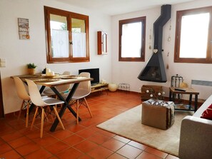 Un salon chaleureux avec une cheminée, un coin repas avec des chaises et une table, et une cuisine équipée d’une cuisinière.