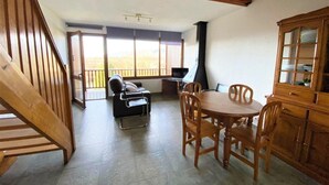 A spacious room with a wooden staircase, a dining area with a table and chairs, a sofa, and a view of the outdoors through large windows. - Duplex 2 rooms 6 Pax, Fireplace, Views, Dishwasher & Washer (Bourg-Madame)