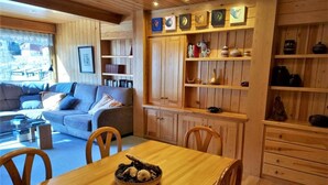 A cozy living room with a wooden dining table, chairs, and a sofa. There are bookshelves and a cabinet with decorative items. - Duplex 3 Bed Parking, Ski Storage & Games Room (La Molina)