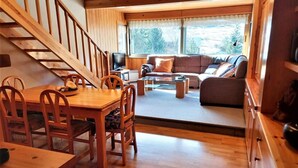 A cozy cabin interior with a wooden dining table, chairs, a sofa, and a TV. - Duplex 3 Bed Parking, Ski Storage & Games Room (La Molina)