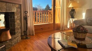 Una habitación acogedora con chimenea de piedra, terraza de madera y un rincón de estar cómodo con lámpara y cesta.