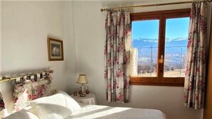 Un dormitorio con cama, mesita de noche, lámpara, ventana con cortinas y un cuadro enmarcado en la pared.