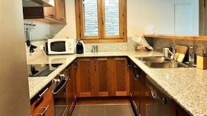 A kitchen with wooden cabinets, a microwave, toaster, and a window above the sink.