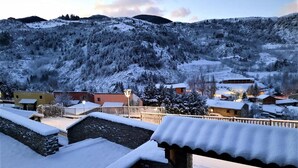 A snow-covered village with traditional buildings, a stone wall, and a view of the surrounding hills.