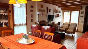Ein gemütliches Wohnzimmer mit Esstisch für zwei Personen, einem Fernseher und einer komfortablen Sitzecke mit Sofa und Sesseln.