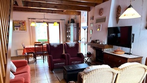 Ein gemütliches Wohnzimmer mit einem roten Sofa, zwei Sesseln, einem Korbstuhl, einem Fernseher und einem Kamin.