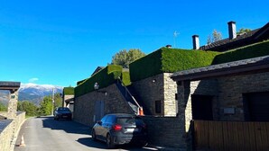 A stone building with a car parked in front, a clear blue sky, and a mountain in the background.