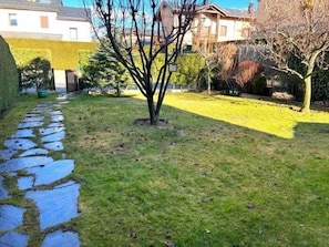 Un jardín con un sendero de piedra, un árbol pequeño y un césped.