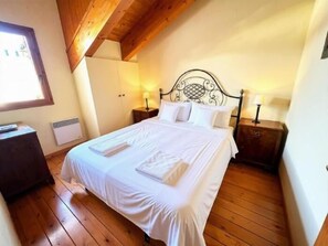 Een slaapkamer met een houten plafond, een bed met witte lakens, twee nachtkastjes met lampen en een raam dat natuurlijk licht binnenlaat.