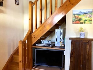 Una escalera de madera que baja a un nivel inferior, donde hay un televisor de pantalla plana y equipo de sonido en un estante.