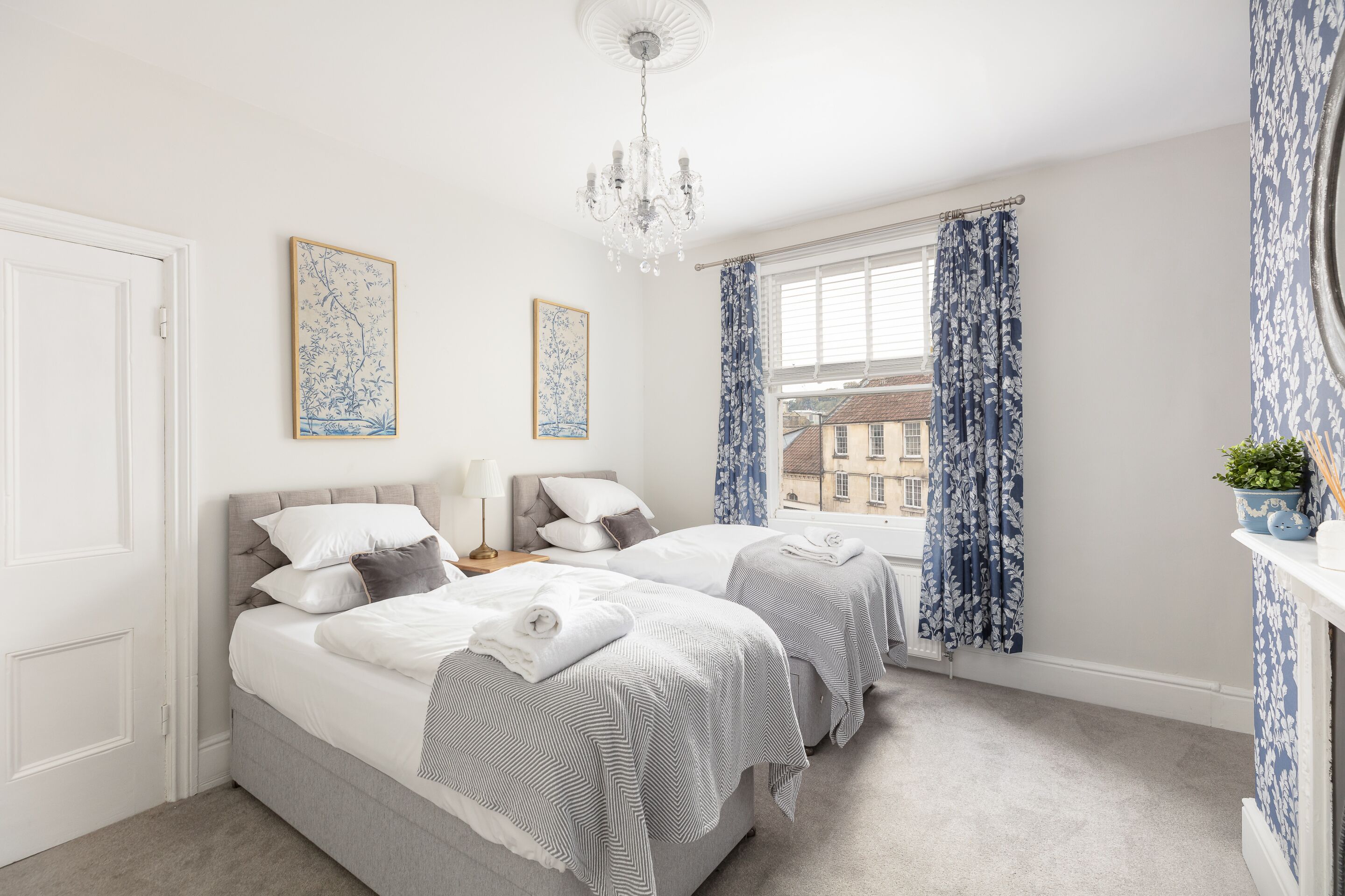 A bedroom with two beds, a chandelier, and a window with curtains.