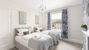 A bedroom with two beds, a chandelier, and a window with curtains.