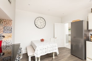 A kitchen with a stainless steel refrigerator, a wall clock, and a table with a patterned tablecloth.