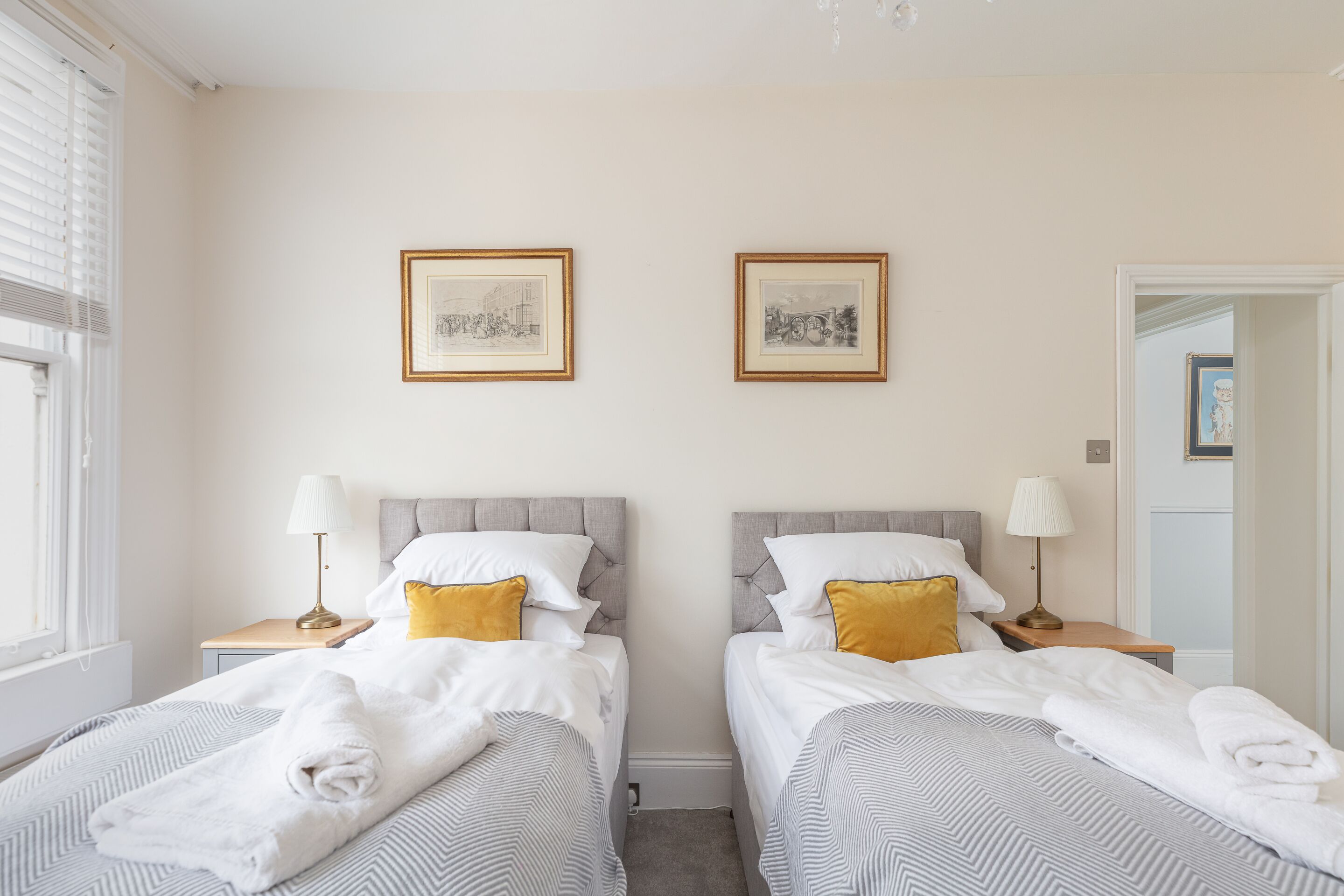 Een hotelkamer met twee bedden, elk met hoofdeind, nachtkastjes, lampen en handdoeken. Er hangen twee ingelijste foto’s aan de muur.