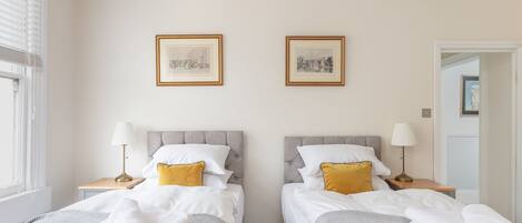 Een hotelkamer met twee bedden, elk met hoofdeind, nachtkastjes, lampen en handdoeken. Er hangen twee ingelijste foto’s aan de muur.