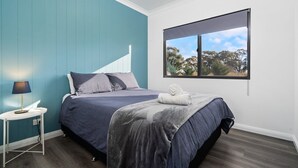 Un dormitorio con cama, mesita de noche, lámpara y ventana con vistas a árboles.