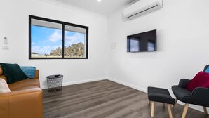 Una habitación moderna con un ventanal grande, un equipo de aire acondicionado, un televisor de pantalla plana y dos sofás.