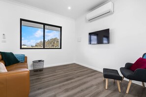 A modern room with a large window, an air conditioning unit, a flat-screen TV, and two sofas.