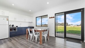 Una cocina moderna con armarios blancos, una mesa de comedor de madera y sillas, y grandes puertas correderas de vidrio que dan a un espacio exterior con césped.