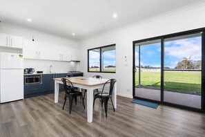 A modern kitchen with white cabinets, a wooden dining table, and black chairs. - Glenowrie Cottage - 1 King, 2 Singles Near Cadia (Forest Reefs)