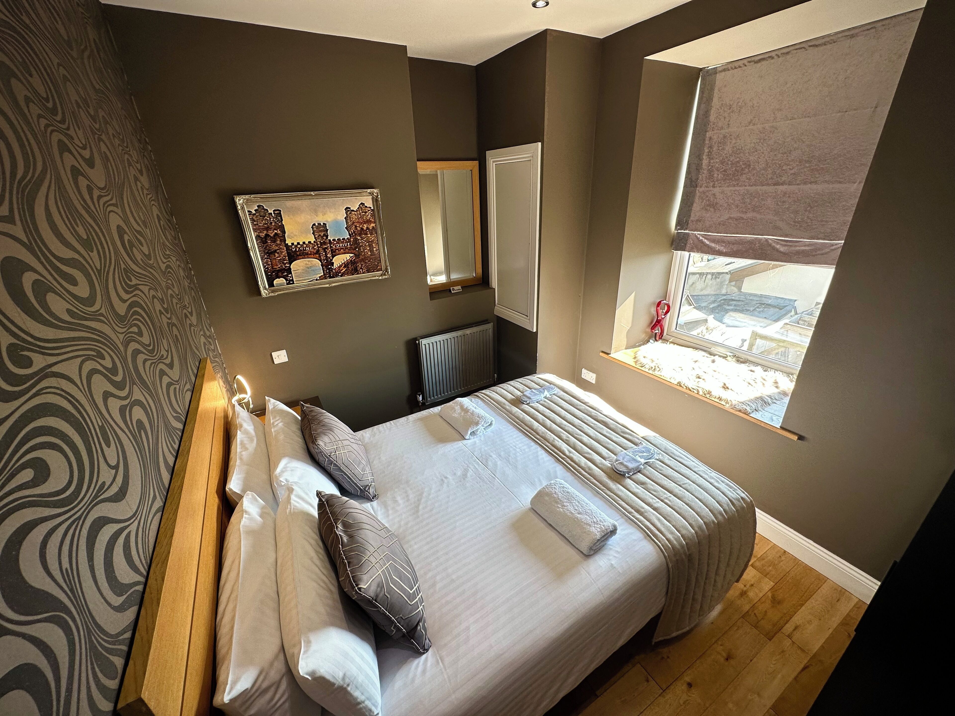 Een slaapkamer met een groot bed, een raam met uitzicht, een radiator en een spiegel aan de muur.