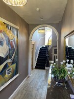 Un pasillo con una escalera, un cuadro abstracto grande y un jarrón con flores blancas.
