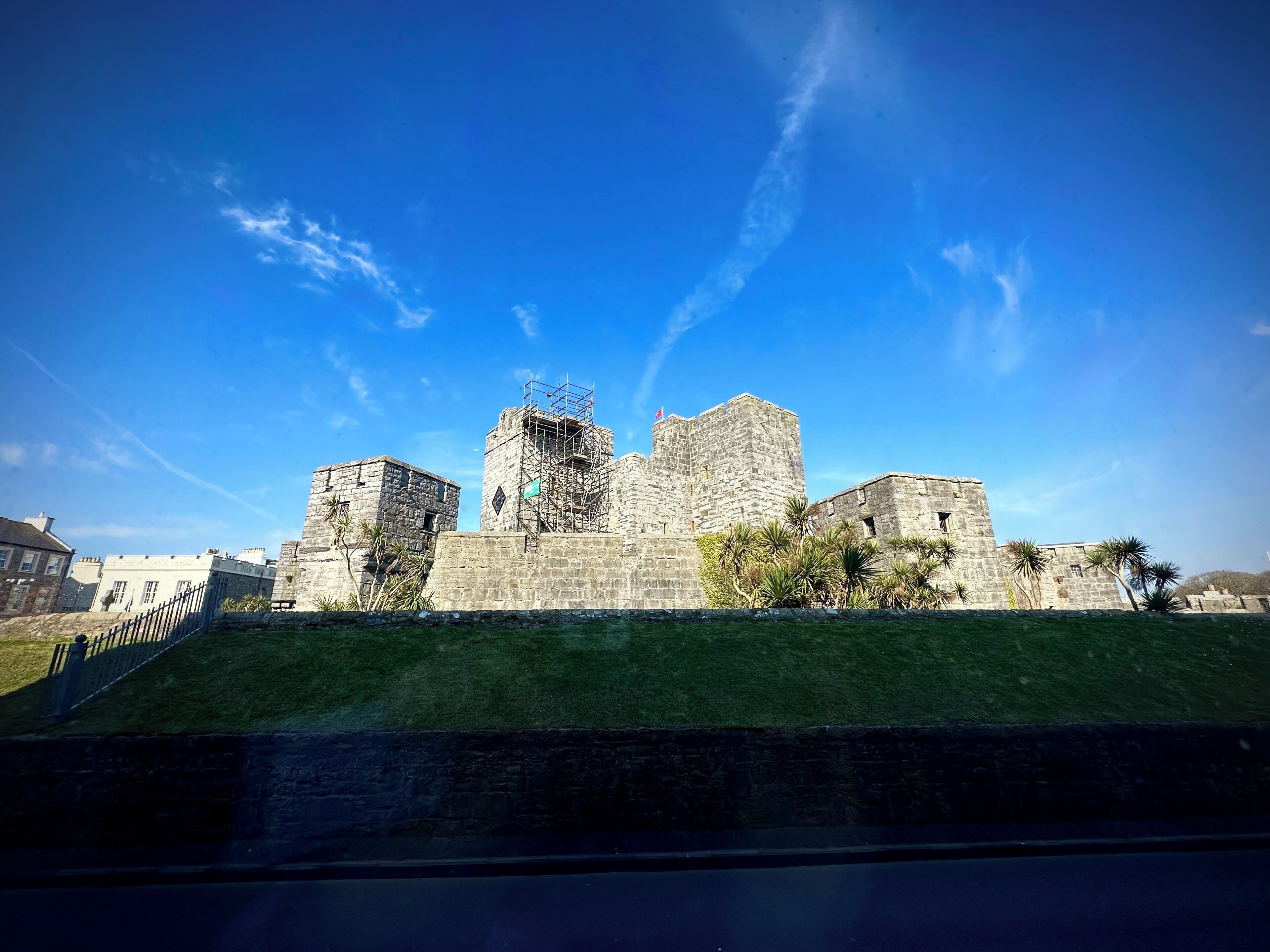Un castillo de piedra histórico con un prado verde y un cielo azul despejado.