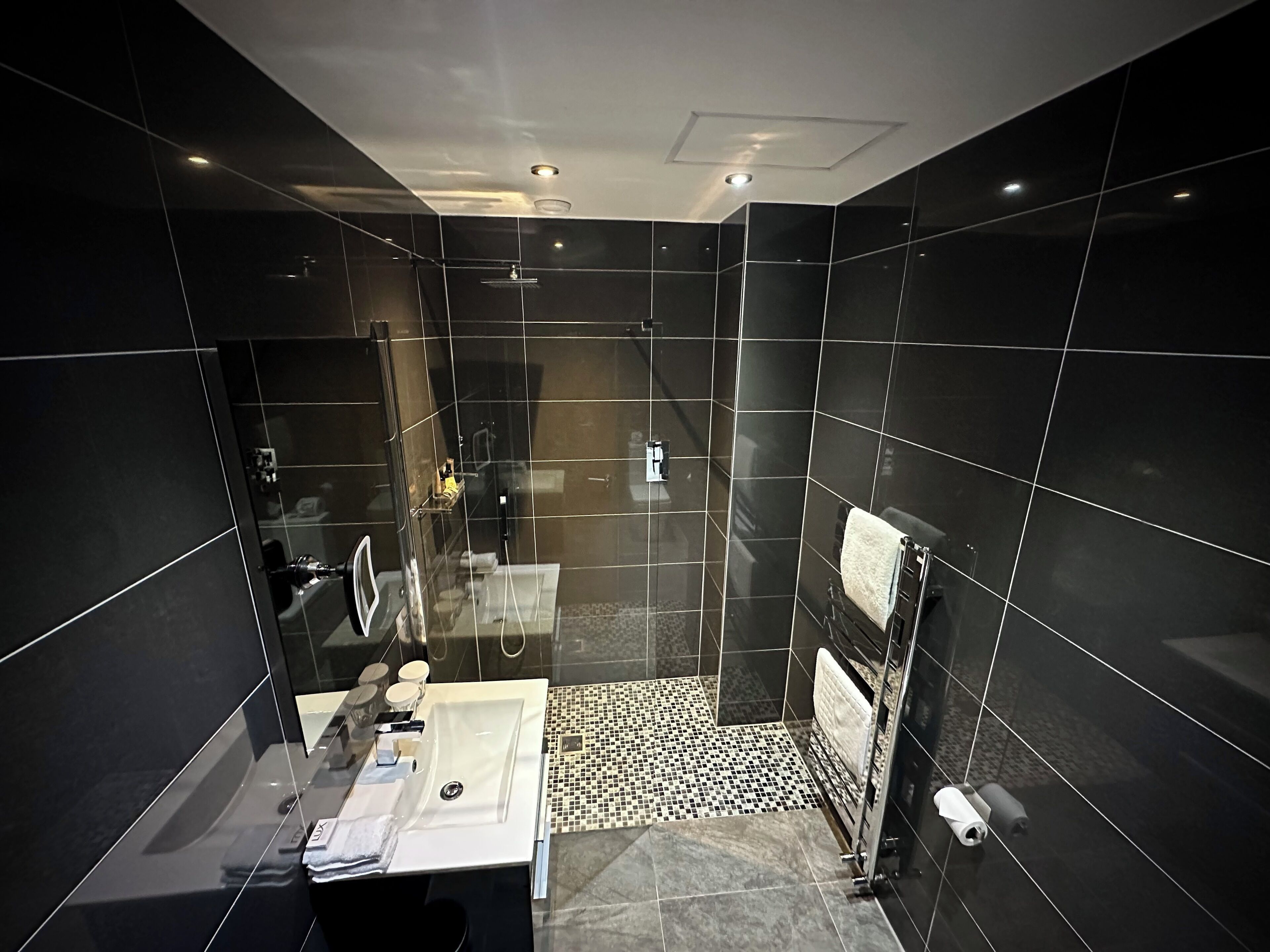 Une salle de bain moderne avec une douche à parois de verre, un lavabo blanc et un sol carrelé en noir et blanc.