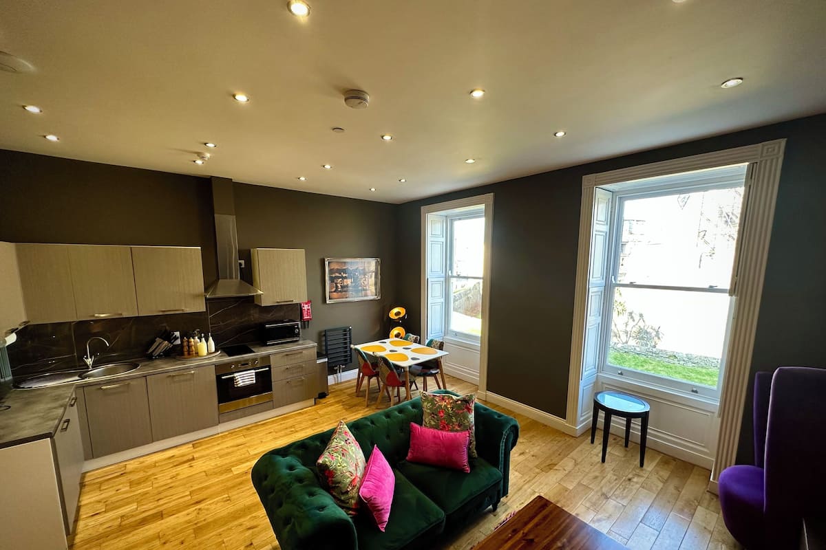 A modern kitchen with a dining area, a green sofa, and a window with a view.