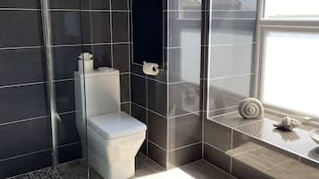 Un baño moderno con azulejos oscuros, cabina de ducha de vidrio, inodoro y ventana con vistas.