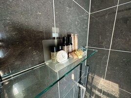 Baño con repisa de vidrio que contiene artículos de aseo.