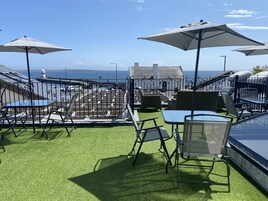 Terraza en la azotea con mobiliario exterior, vista al mar y un faro al fondo.